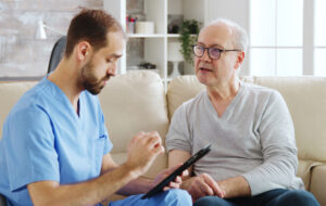 Caucasian male nurse talking with a nursing home patient about his health. The nurse is making notes on a digital tablet