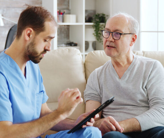 Caucasian male nurse talking with a nursing home patient about his health. The nurse is making notes on a digital tablet