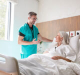 Surgeon Visiting And Talking With Mature Female Patient In Hospital Bed