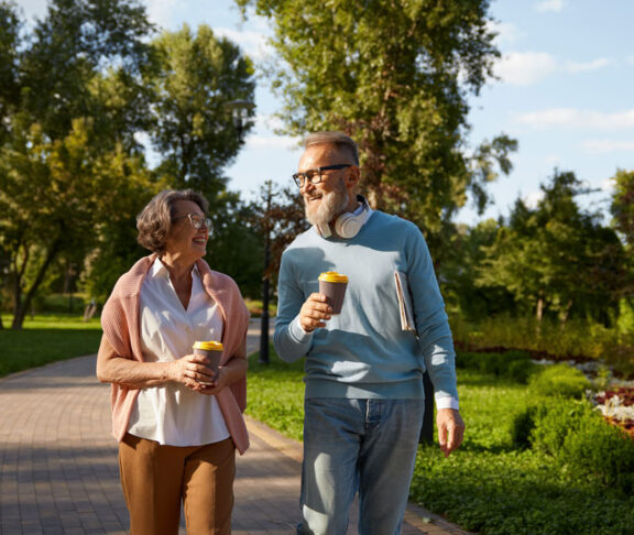Happy elderly couple having coffee break walking in park
