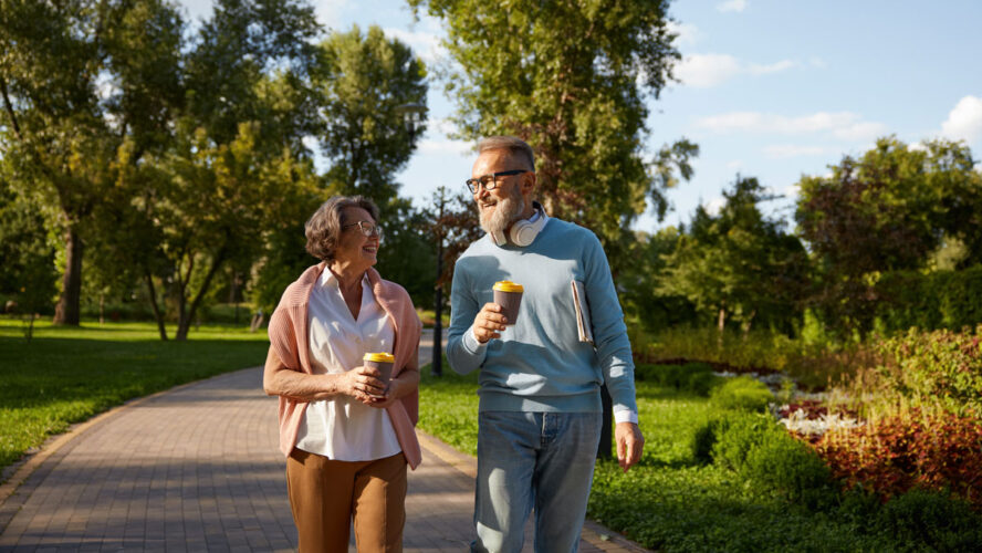 Happy elderly couple having coffee break walking in park