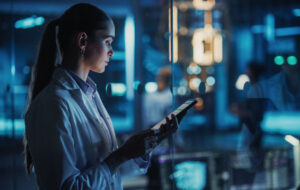 Female Scientist Using a Tablet to Monitor the Work of a Quantum Computer, Focusing on Data Flow, Compute and Hardware Stability. Futuristic Dark Setting with Advanced Technological Office
