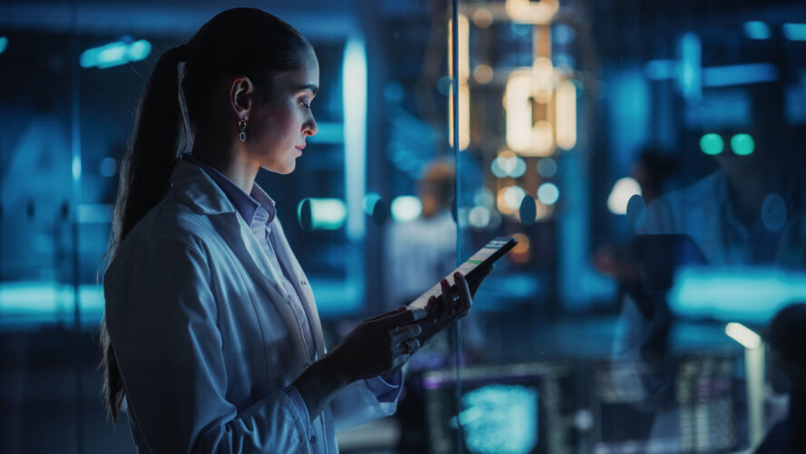 Female Scientist Using a Tablet to Monitor the Work of a Quantum Computer, Focusing on Data Flow, Compute and Hardware Stability. Futuristic Dark Setting with Advanced Technological Office