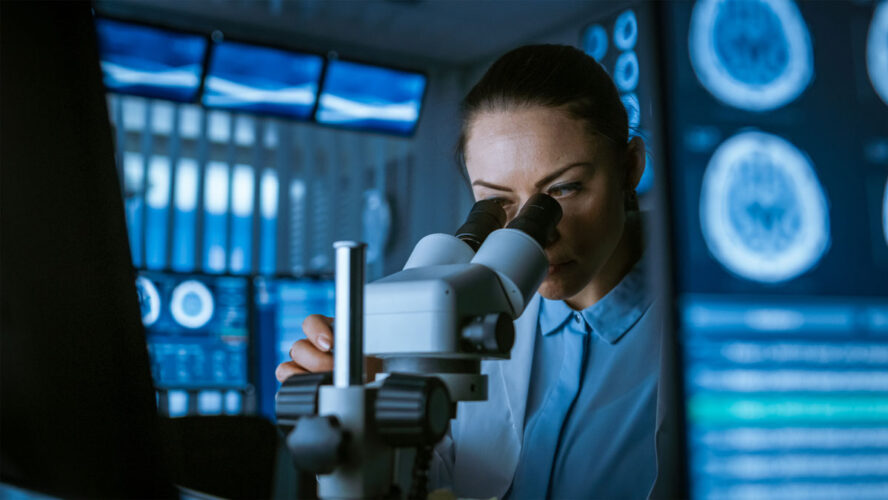 Female Medical Research Scientist Looking Through the Microscope Types Acquired Data in the Computer. Laboratory. In the Laboratory with Multiple Screens Showing MRI / CT Brain Scan Images