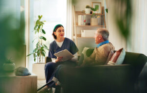 Caregiver, clipboard and senior man on sofa for assisted living, medical service and diagnosis in nursing home. Retirement, healthcare and nurse with elderly person for consulting, support and help