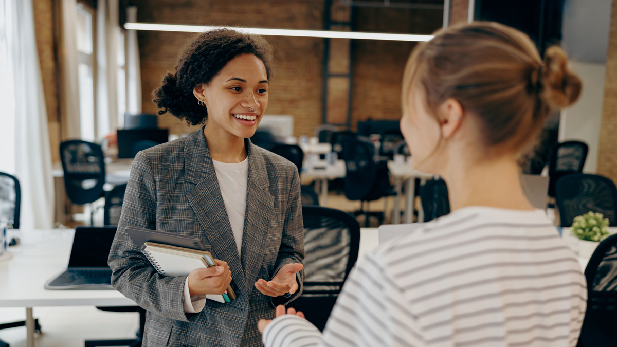 Two young diverse business women chatting during work break standing in modern office