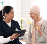 Tablet, nurse and woman with cancer patient, elderly and hospital consultation for wellness. Tech, happy and medical professional with sick senior person coughing for advice, healthcare or support