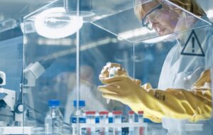 Senior Female Epidemiologist Works with Samples in Isolation Glove Box. She's in a Modern, Busy Laboratory Equipped with State of the Art Technology