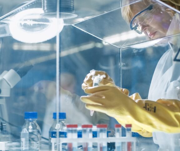 Senior Female Epidemiologist Works with Samples in Isolation Glove Box. She's in a Modern, Busy Laboratory Equipped with State of the Art Technology