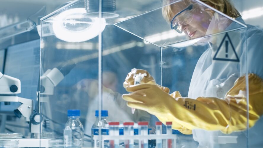 Senior Female Epidemiologist Works with Samples in Isolation Glove Box. She's in a Modern, Busy Laboratory Equipped with State of the Art Technology