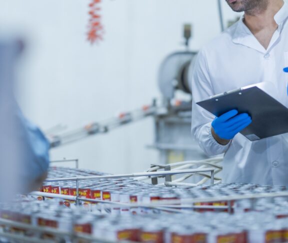 A food processing supervisor wearing protective gear and holding a clipboard, inspecting machinery on a production line, emphasizing quality control, safety, and efficiency in industrial operations