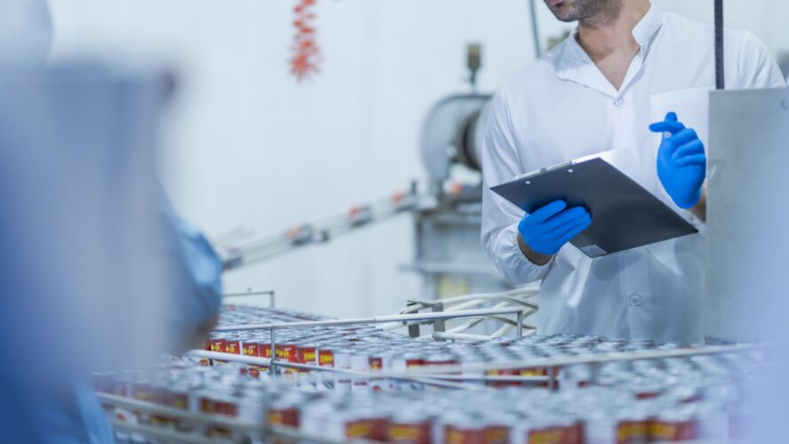 A food processing supervisor wearing protective gear and holding a clipboard, inspecting machinery on a production line, emphasizing quality control, safety, and efficiency in industrial operations