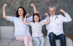 Happy family doctor, girl patient and mother showing strong gesture by arm
