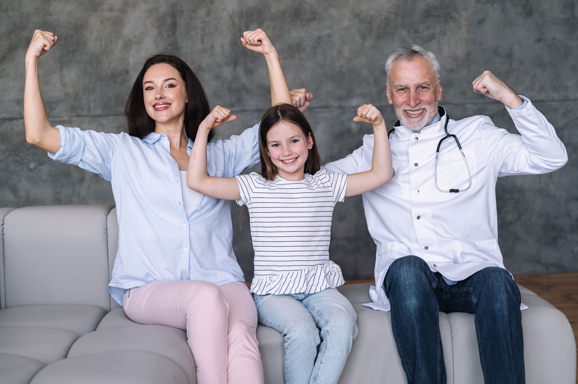 Happy family doctor, girl patient and mother showing strong gesture by arm