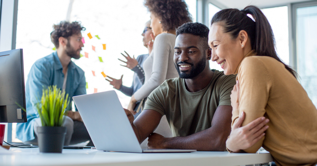 A man and a woman in an office look at a laptop screen together smiling