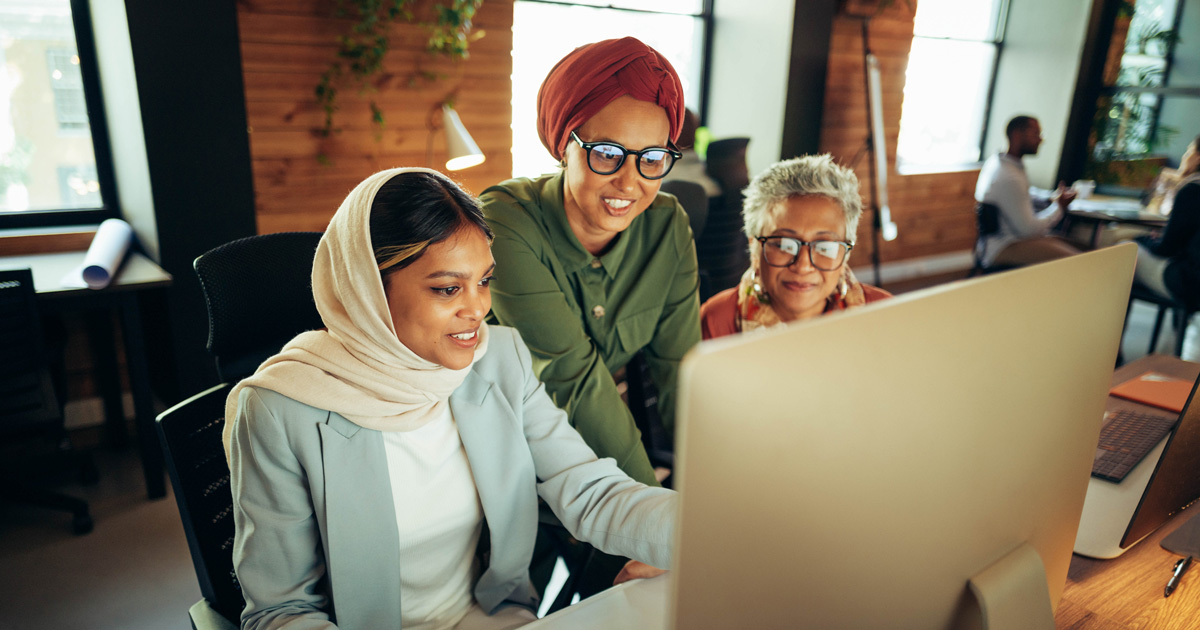 Three cheerful businesswomen having a discussion while looking at a computer screen in an office.