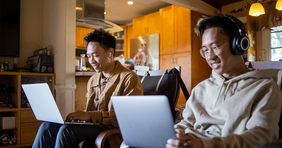 brothers doing separate tasks on their computers together in the living room