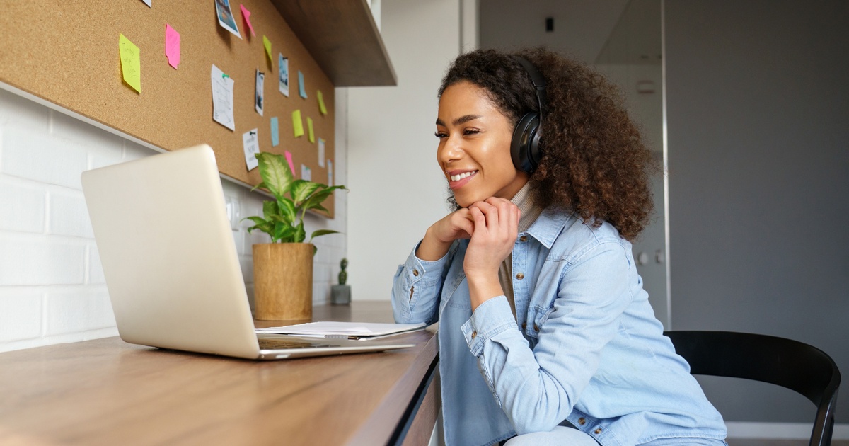 Smiling young african american teen girl wear headphones video calling on laptop. Happy mixed race pretty woman student looking at computer screen watching webinar or doing video chat by webcam.