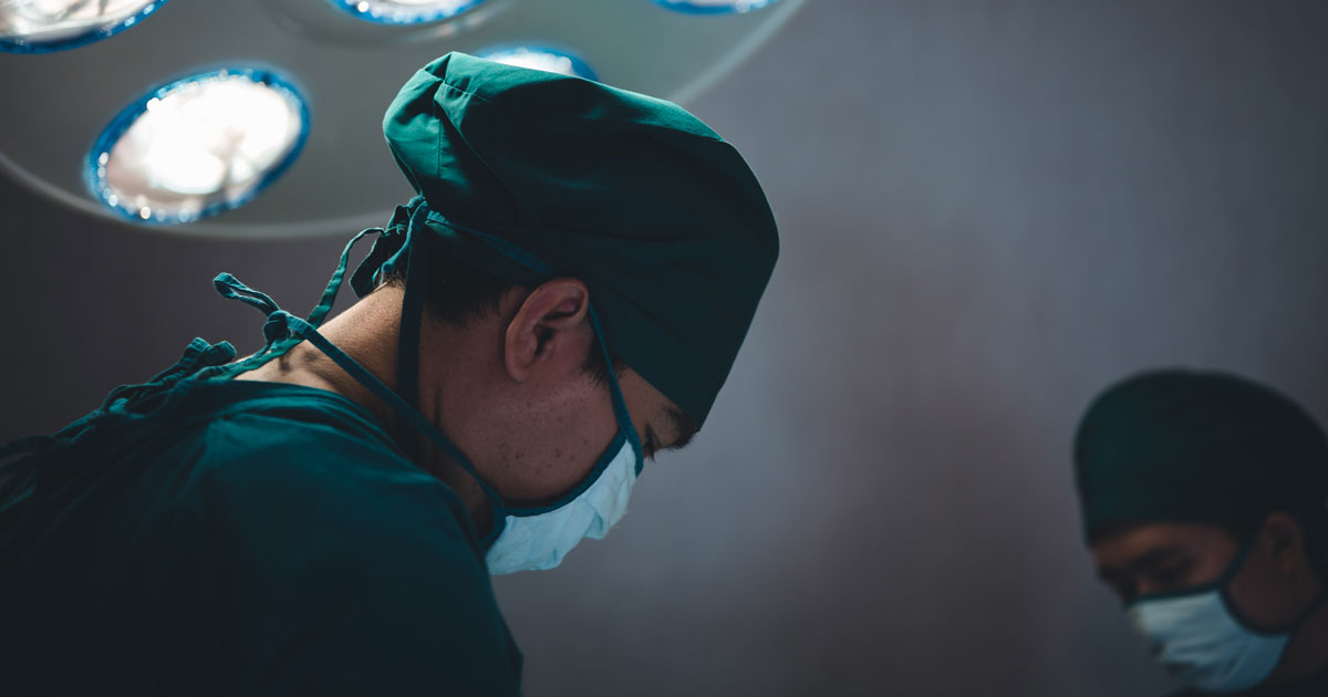 Team of doctors wearing protective clothing works together to monitor patients in Bright Modern operating room