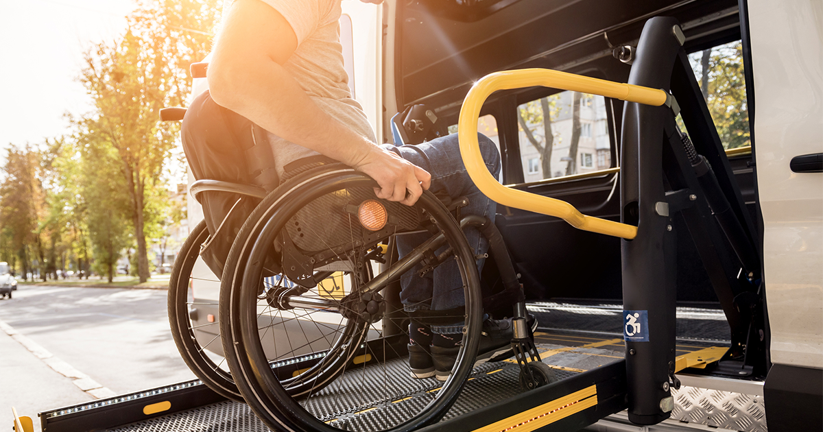 A man in a wheelchair on a lift of a vehicle for people with disabilities.