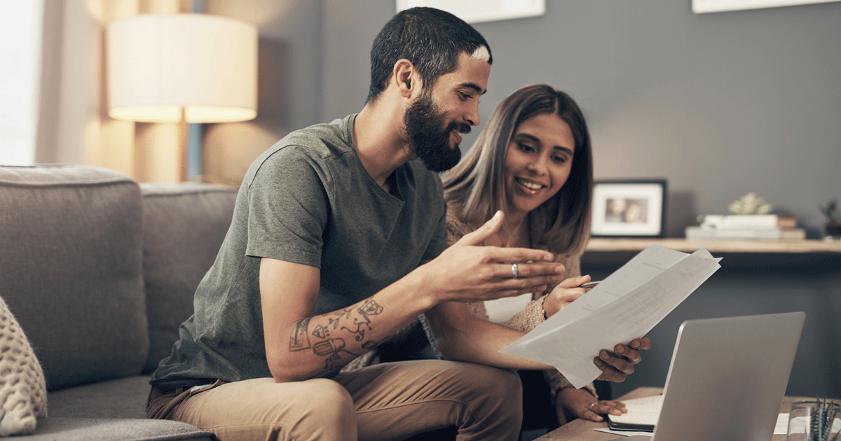 Shot of a young couple using a laptop while going through paperwork at home