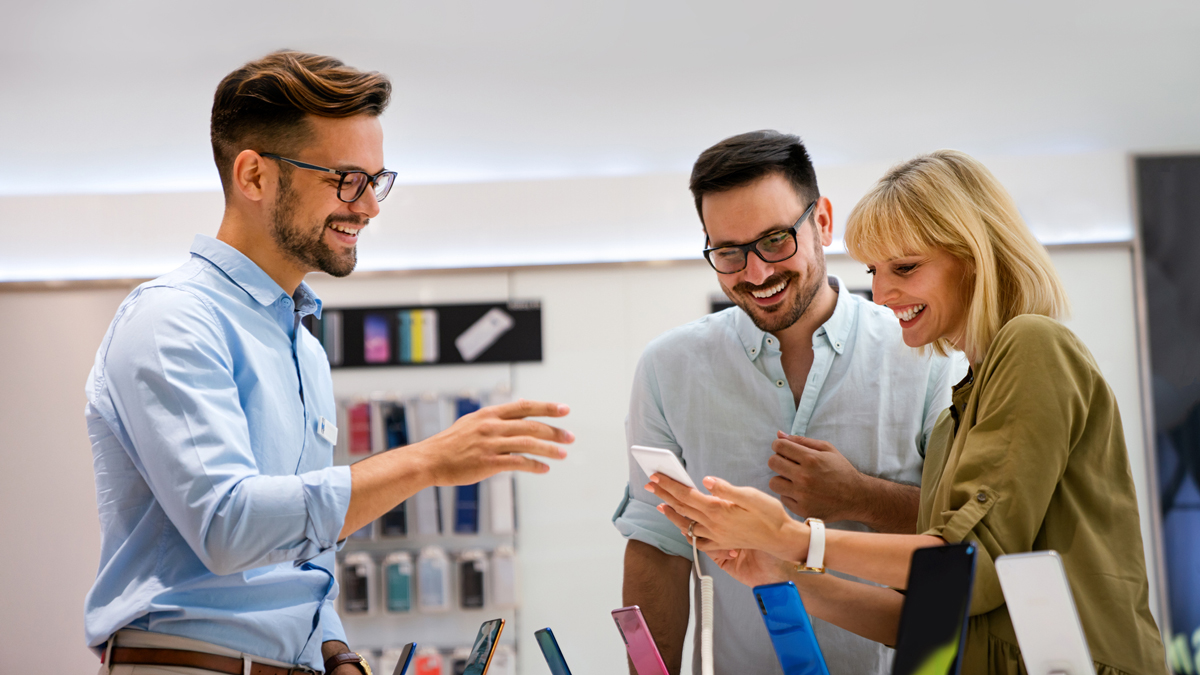 Portrait of salesman helping to people to buy a new digital device in tech shop.