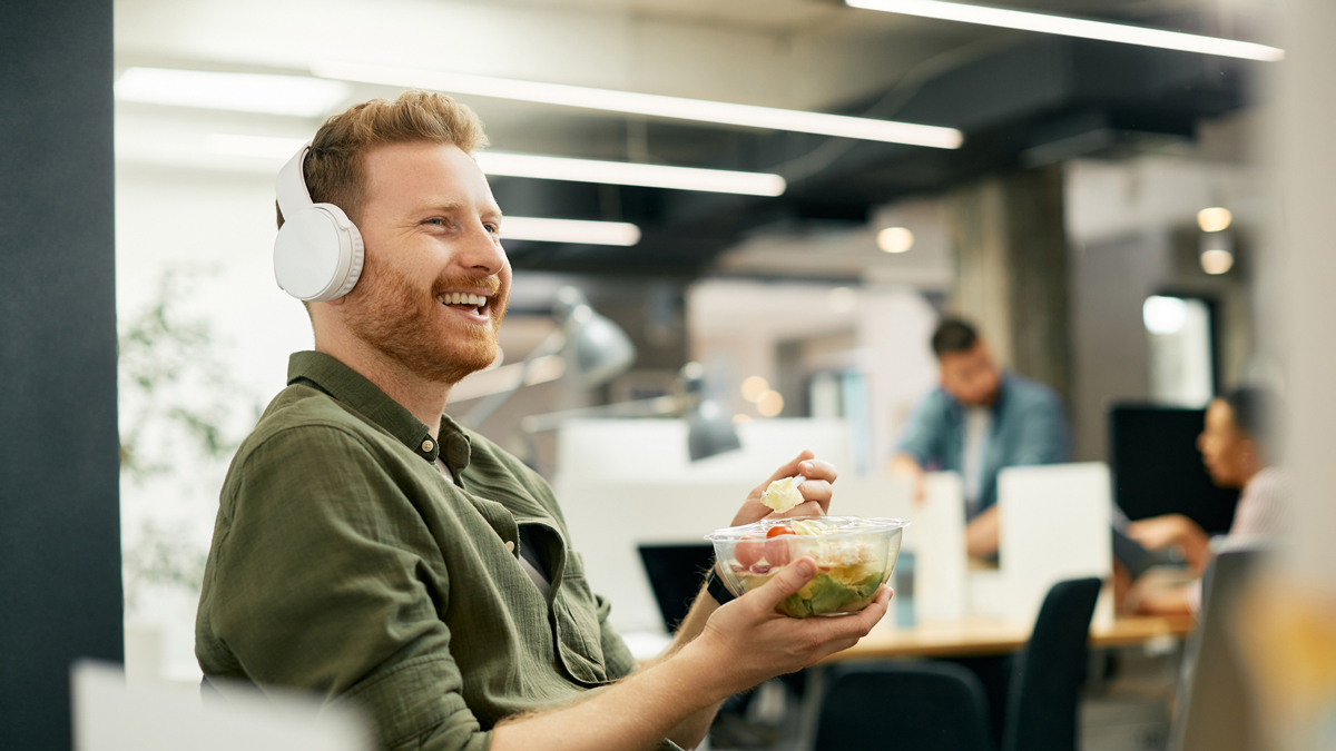 Happy freelance worker listening music while having lunch break at corporate office. - stock photo
