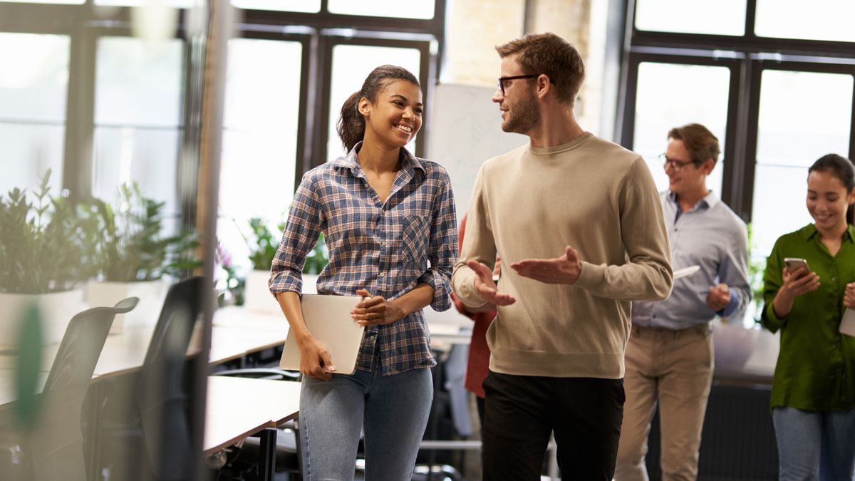 Two young diverse business people, male and female coworkers talking, discussing project and smiling while walking down the modern office
