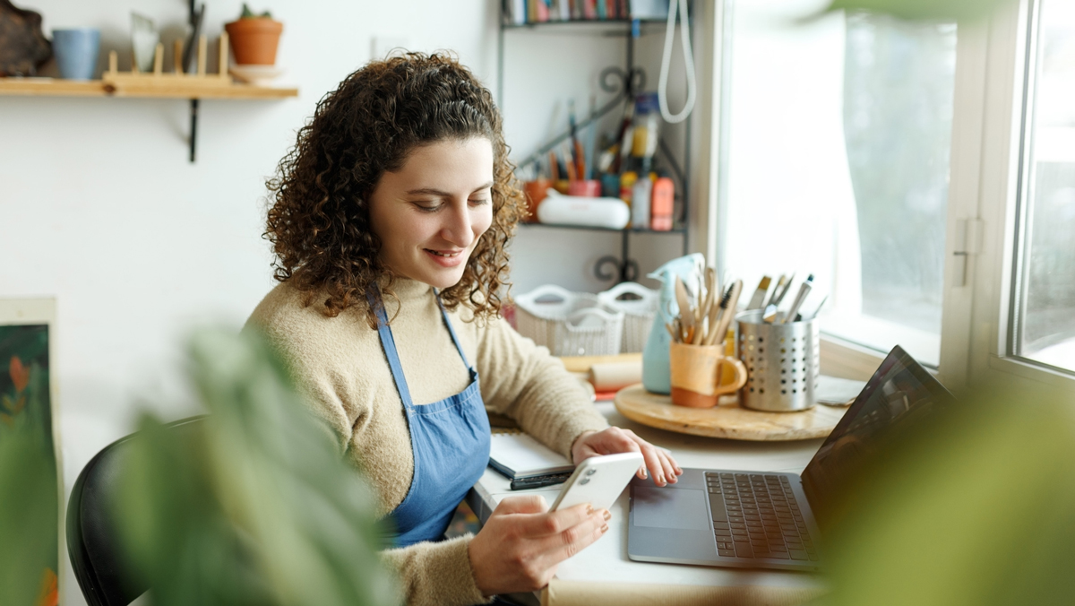 Female ceramist reading a text message on her smartphone. Creative businesswoman managing a store with a collection of ceramic products. Young entrepreneur running a successful small business.