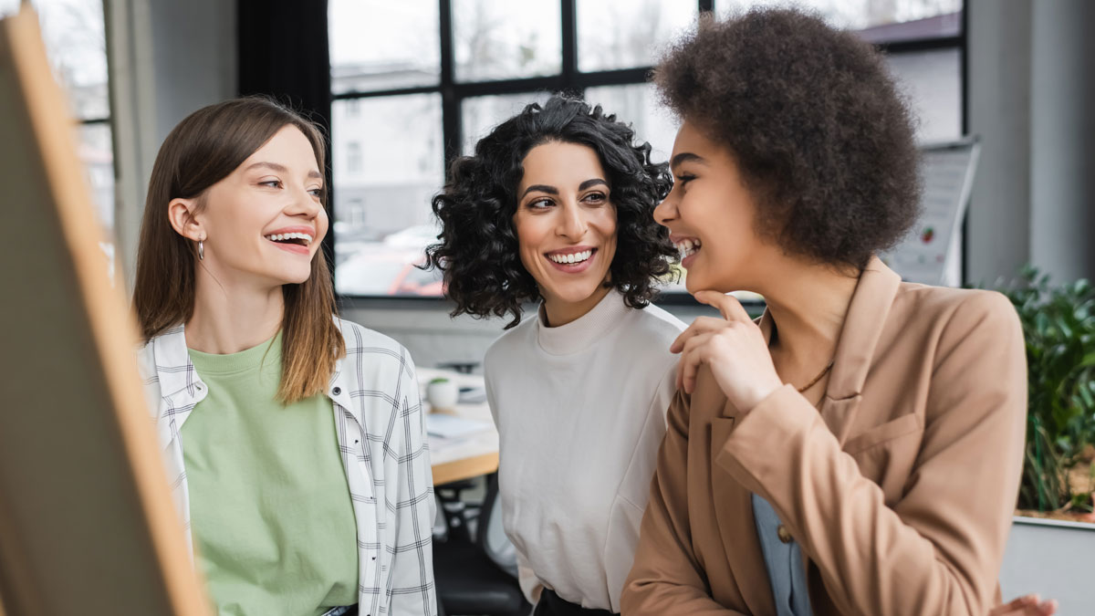 Cheerful interracial businesswoman talking near blurred board in office