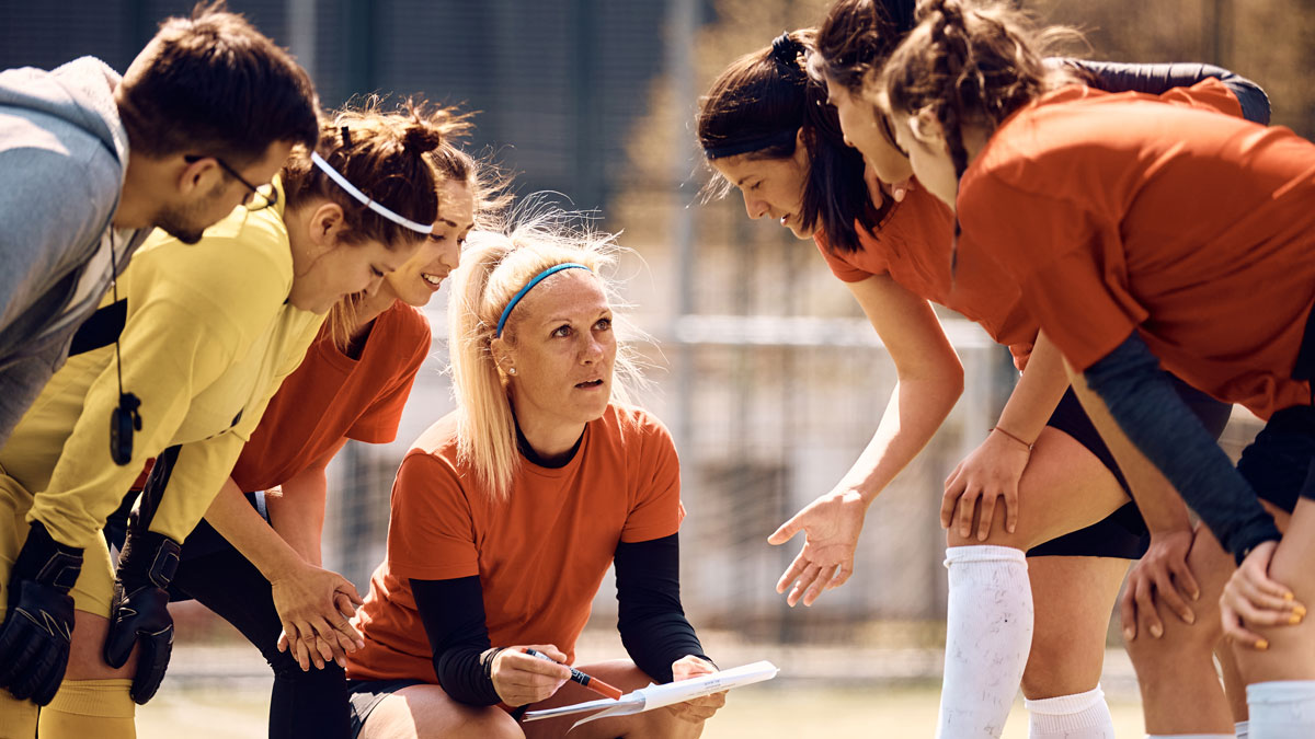 Women's soccer team and their coach going through game plan on football pitch.