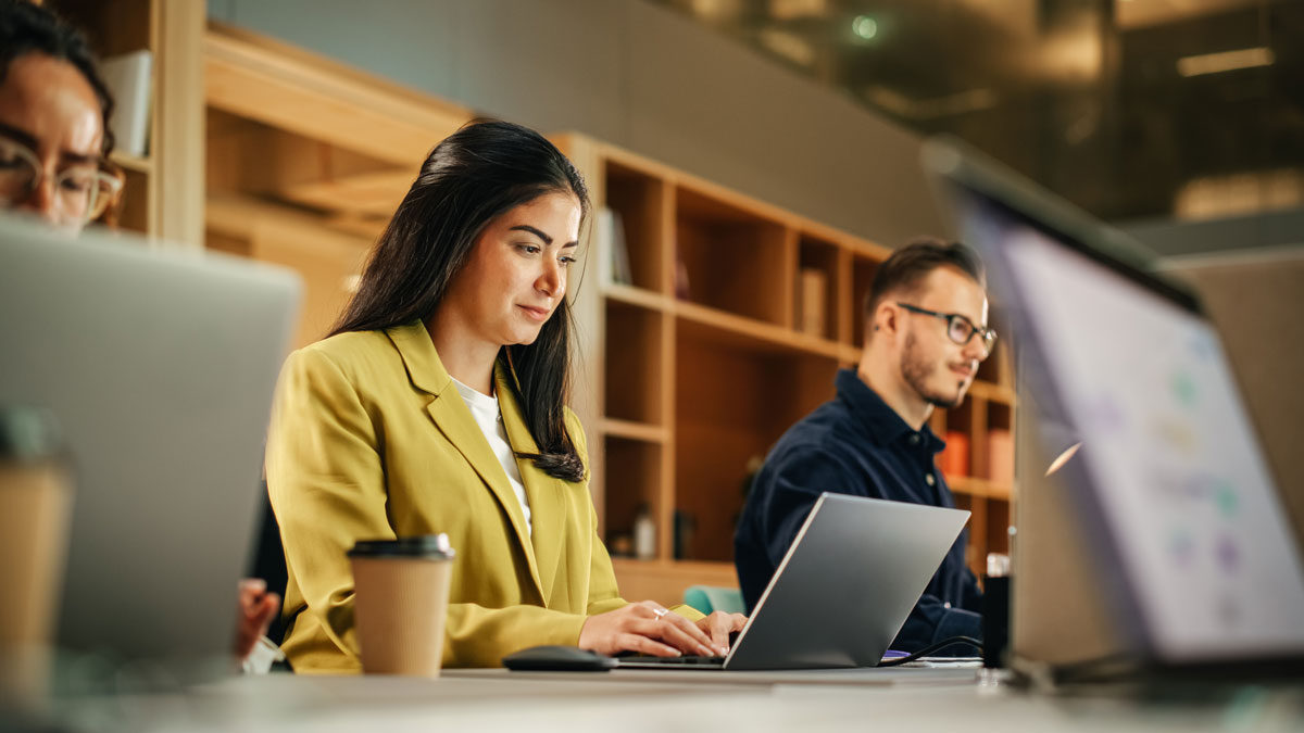 Group of Diverse Creative Team Members Using Laptops in an active Contemporary Office. Young Female Media Relations Manager Working on Brand Innovation Strategy and Collaborating with Colleagues
