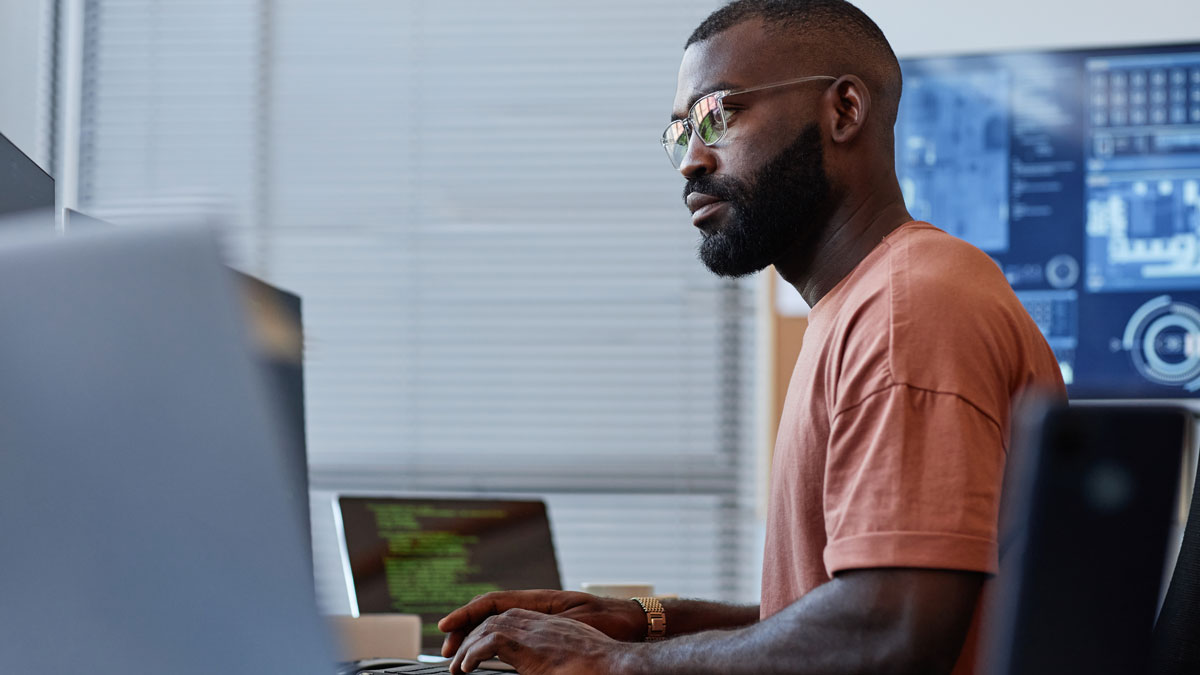Side view portrait of black software developer using computer in high technology office, data systems and programming