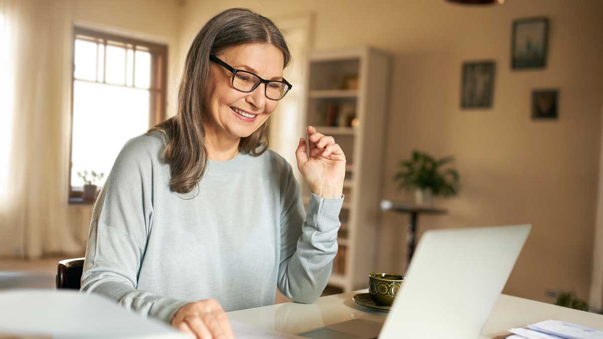 Beautiful retired female using portable computer for remote work. Cheerful elderly woman enjoying online communication, talking to son via virtual chat on laptop. Aged people and electronic devices