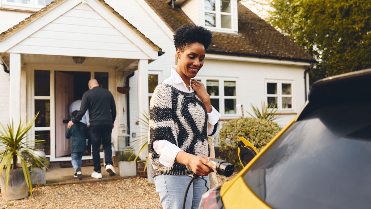 Woman plugging in electric charger into car with family outside home