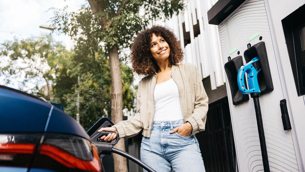 Smiling woman charges an electric vehicle at a public charging station, showcasing sustainable and eco-friendly transportation in a modern urban setting
