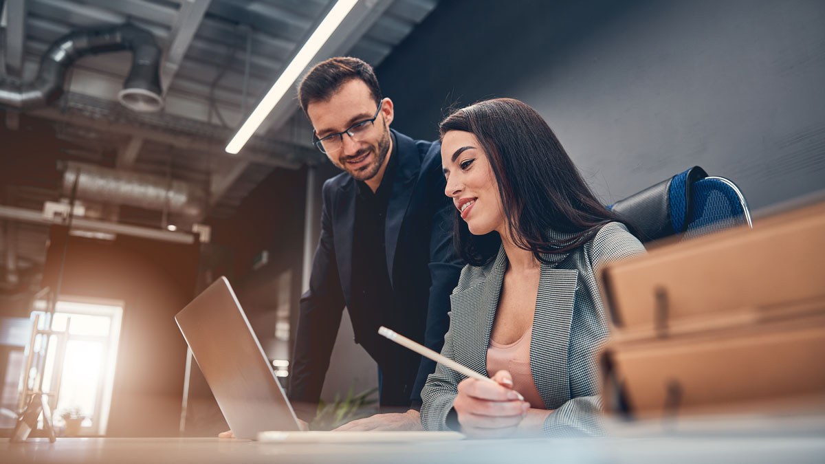 Smiling co-workers looking at laptop while discussing contract