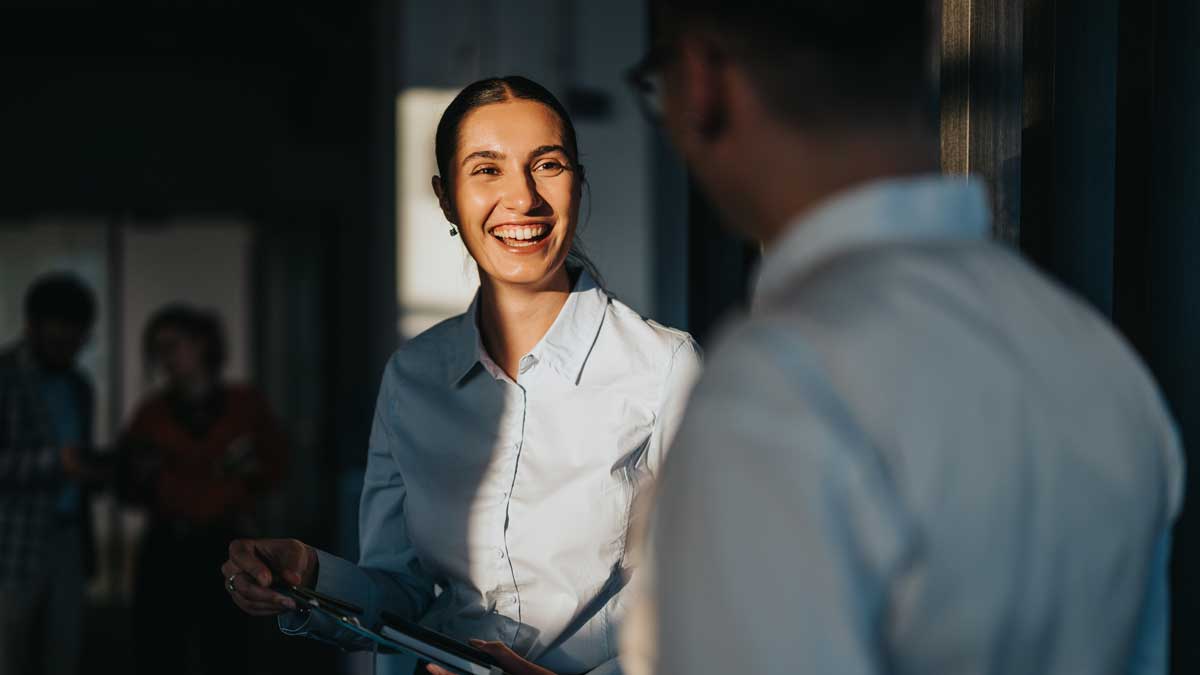 A diverse group of business people engaging in a friendly conversation in an office hallway. The image captures a positive and collaborative work environment with multicultural colleagues