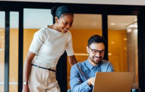 Smiling colleagues discussing ideas together at an office using a laptop