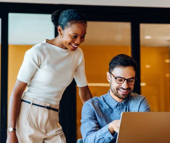 Smiling colleagues discussing ideas together at an office using a laptop