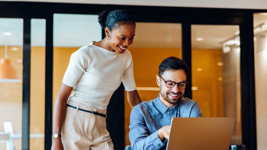 Smiling colleagues discussing ideas together at an office using a laptop