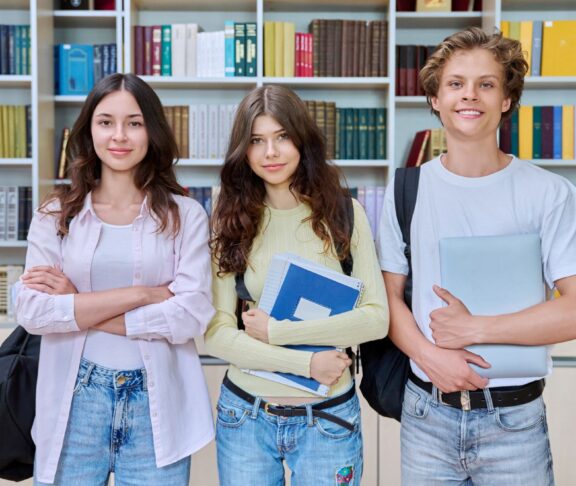 Portrait of three teenage students, smiling teenagers guy and girls looking at camera in classroom