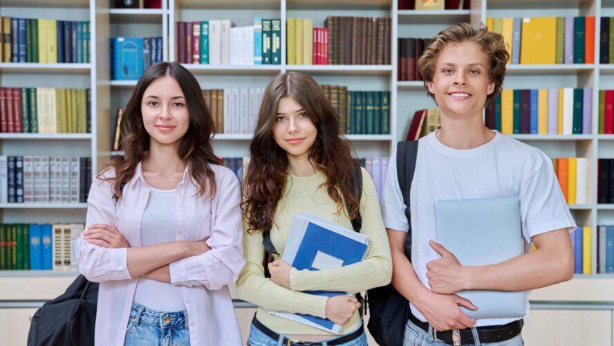 Portrait of three teenage students, smiling teenagers guy and girls looking at camera in classroom