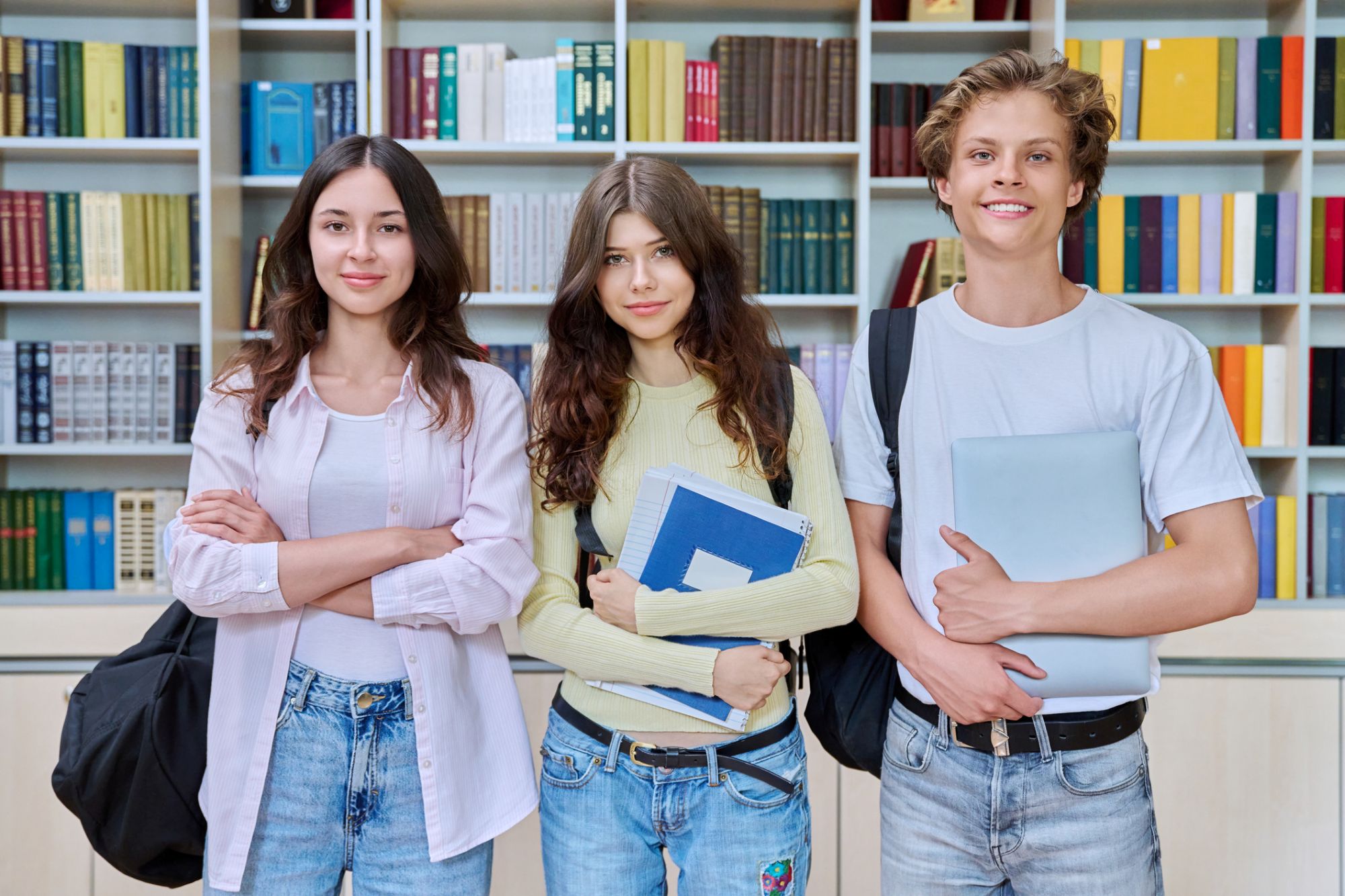 Portrait of three teenage students, smiling teenagers guy and girls looking at camera in classroom