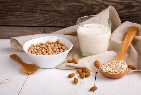 Vegan non dairy milk in glass and milk alternatives ingredients like a nut, almond, soy, oat on wooden table with kitchen towel. Organic food and drink, health care, diet and nutrition concept.