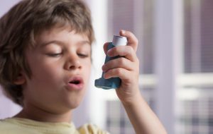 Boy using asthma inhaler to treat inflammatory disease, wheezing, coughing, chest tightness and shortness of breath. Allergy treating concept. Selective focus on inhaler.