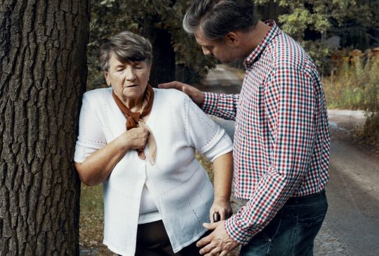 Helpful pedestrian taking care of senior woman having heart attack on the street