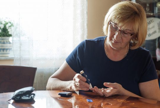 Senior woman in her 60s using sugar blood test to check the sugar level in blood stream. Woman is living life with chronic illness everyday and overcoming challenges that illness brings.