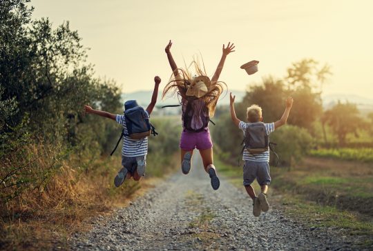 Brothers and sister hiking in Tuscany, Italy. Kids are jumping with joy on dirt road.