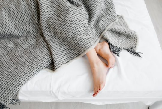 Female feet under blanket flat lay. Female beautiful feet with red pedicure on the bed. Top view on the sleeping woman legs under gray blanket